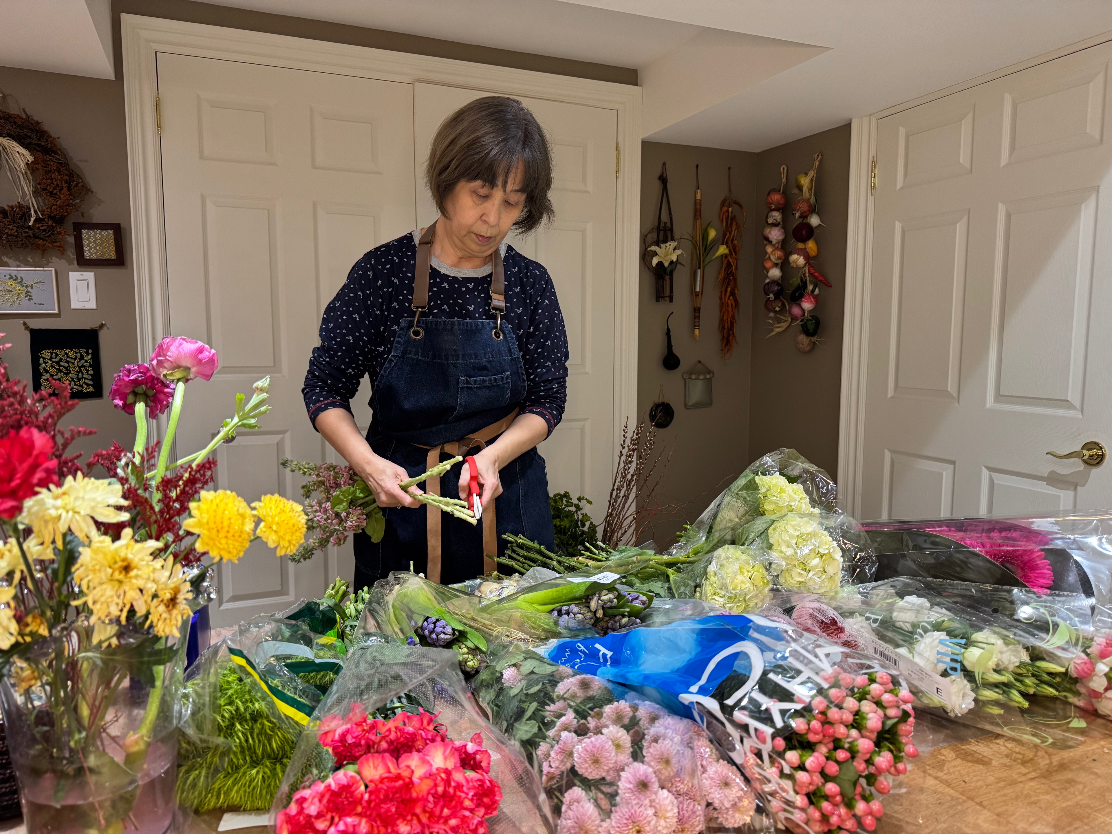 Woman arranging flowers in a home setting with various floral arrangements on a table Sakagen F-170 Flower Scissors